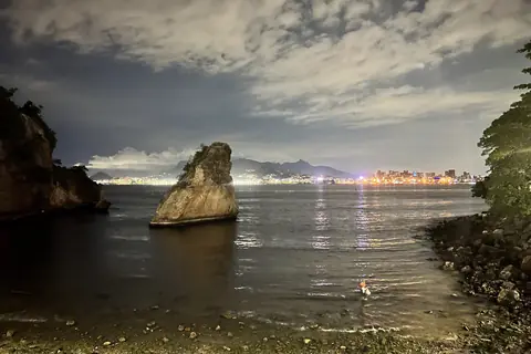 Felsen im Wasser am Strand von Boa Viagem in Niterói, dahinter die Lichter der Stadt