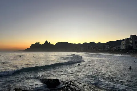 Wellen am Arpoador bei Sonnenuntergang mit dem Morro Dois Irmãos in der Ferne